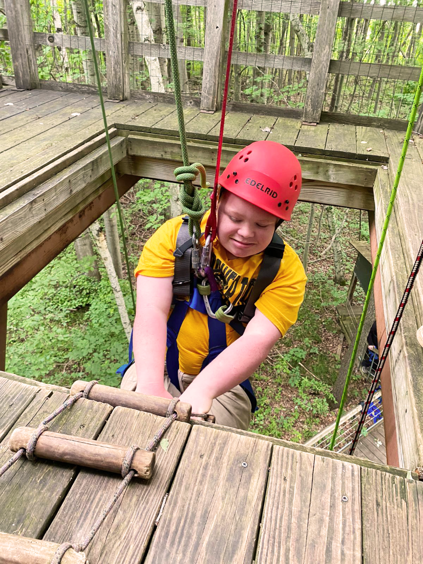 A boy climbs the treehouse with the help of ropes. 