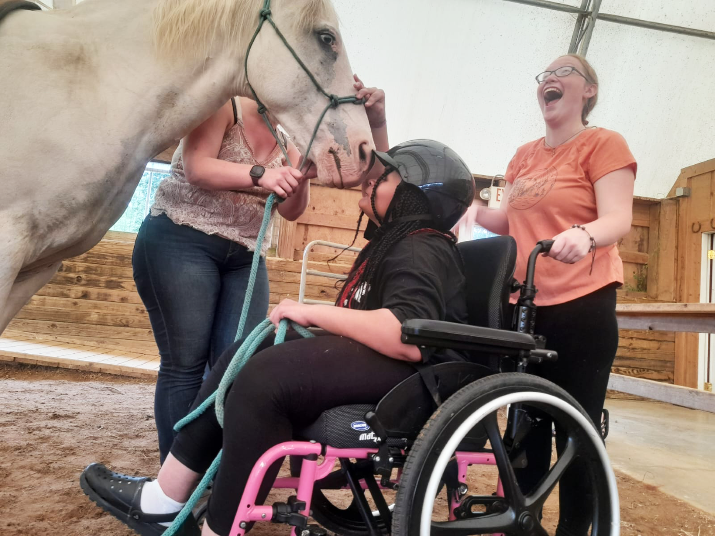 A camper in a wheelchair gets a kiss from one of the horses at The Fowler Center