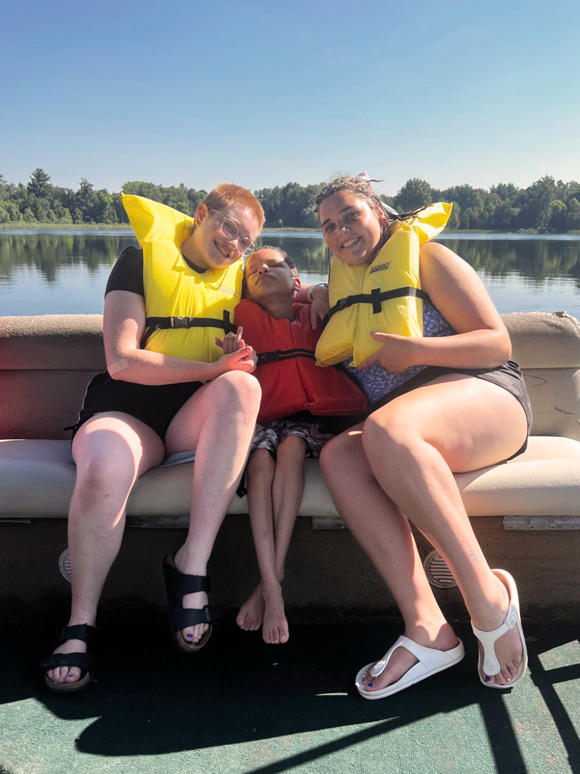 Two counsellors sit with a young boy on a boat during our seasonal summer camp.