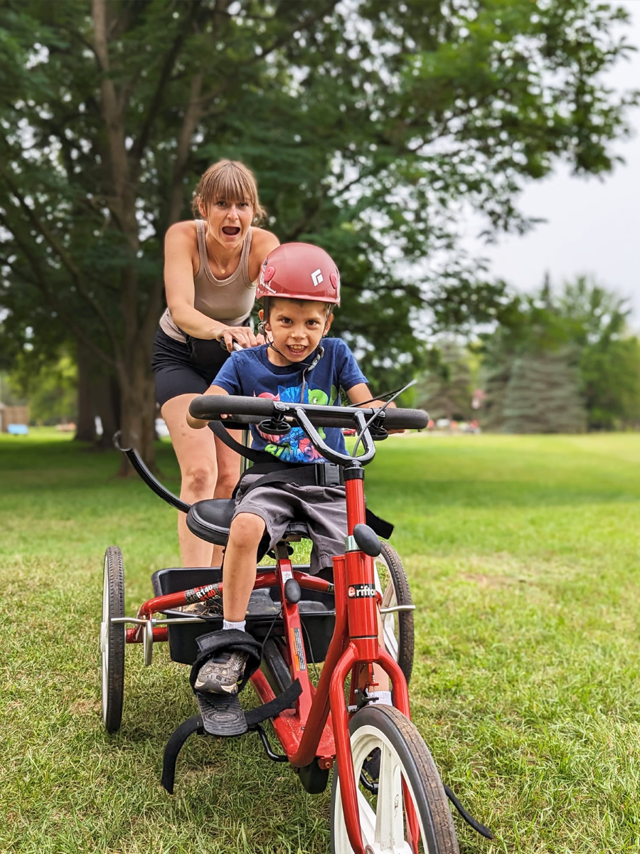 A camp counsellor pushes a little boy in a tricycle at The Fowler Center