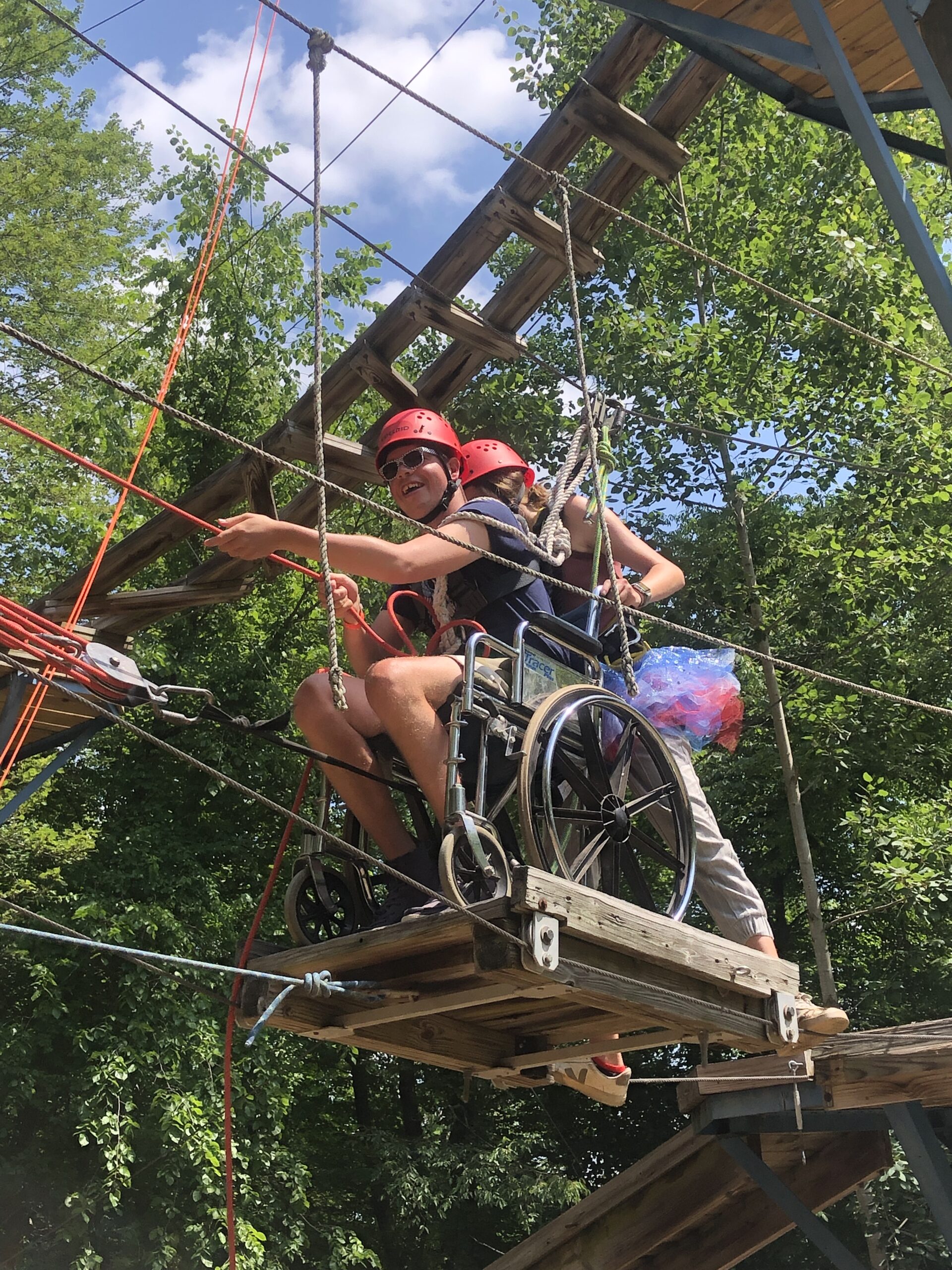 A camper in a wheelchair crosses the ropes on the high ropes course during Camp Barefoot