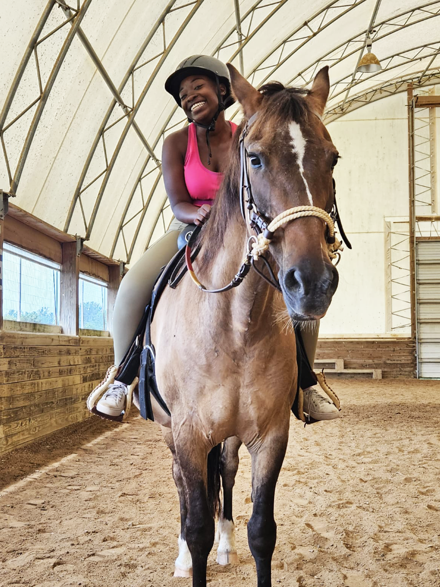 A young girl is smiling while she rides one of the horses at The Fowler Center